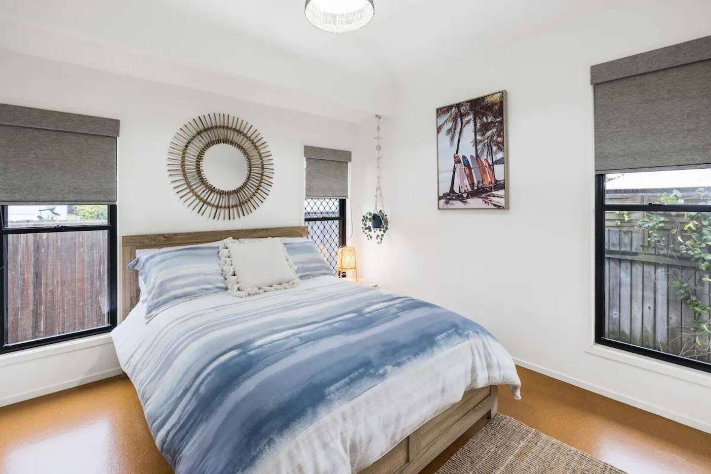 Double bed with striped blue bedding beside garden-facing windows