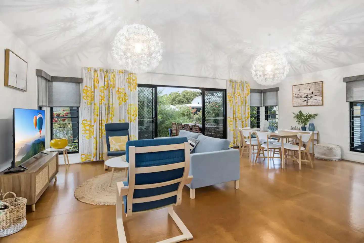 Open-plan living and dining room with high white ceilings, timber floors and blue kitchen cabinetry