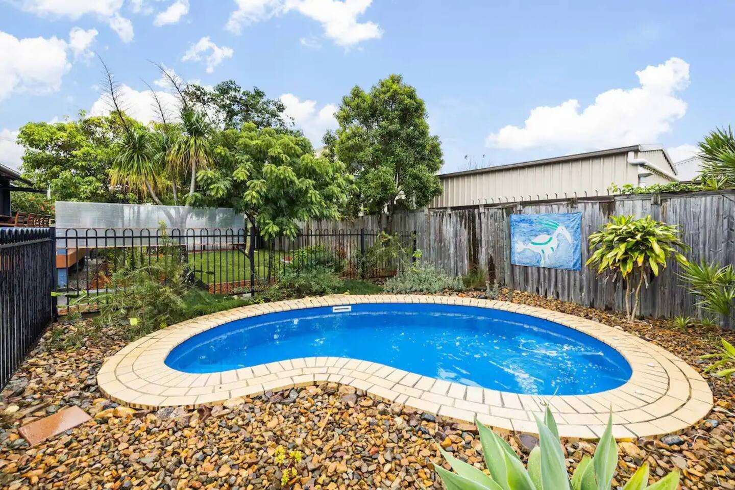 Private circular blue pool surrounded by palms and a timber fence