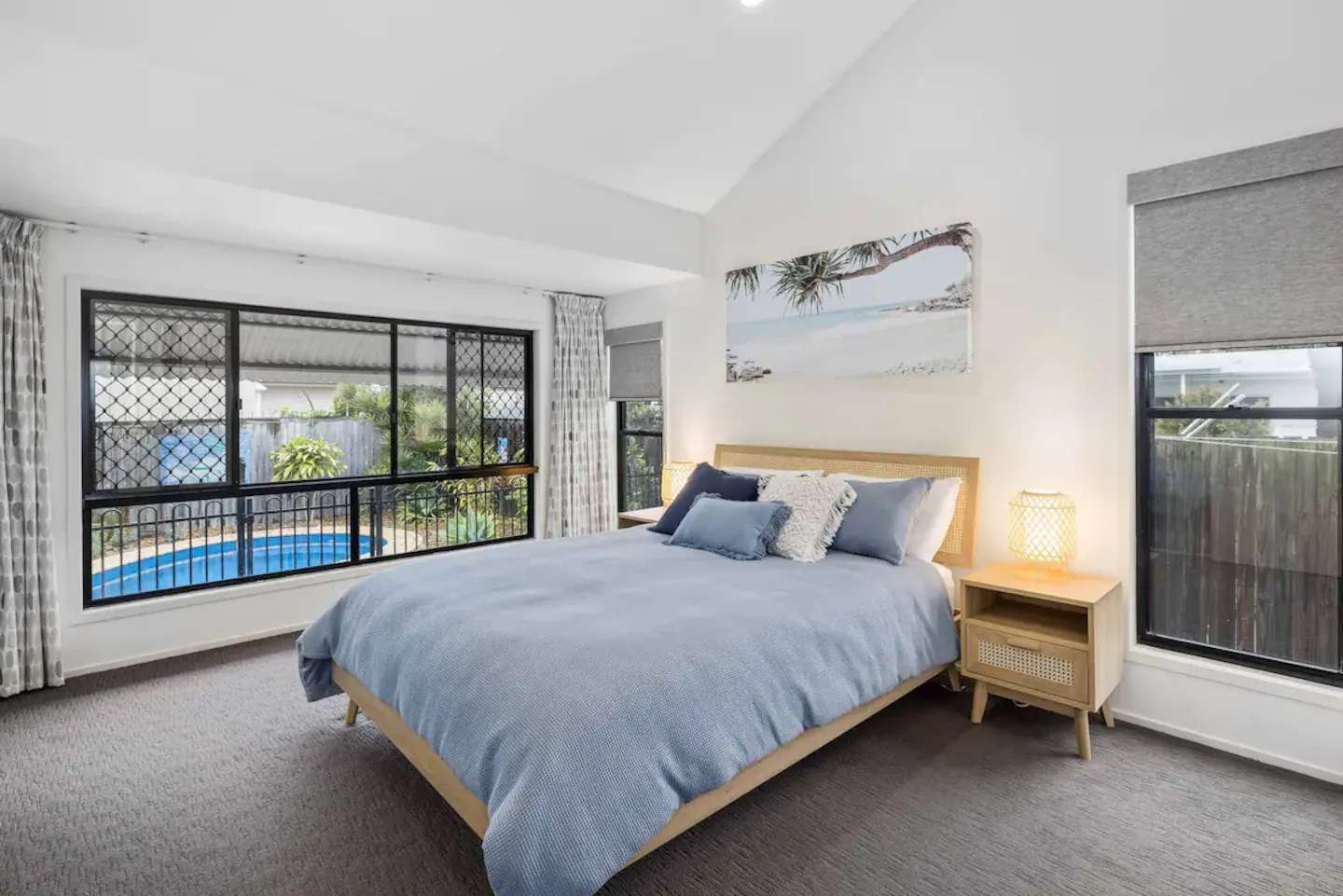Queen bed with blue bedding and windows overlooking the pool